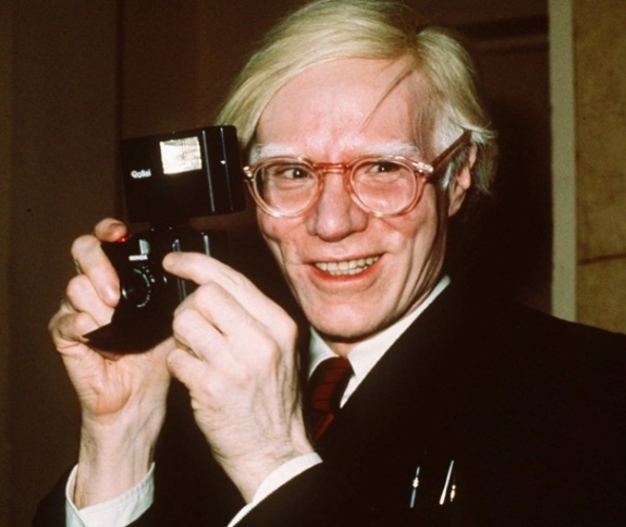 Pop artist Andy Warhol smiles in New York in this 1976 file photo. Known for his pop art and quips about fame, the National Gallery’s exhibit is the first to focus on Warhol’s interest in news media.