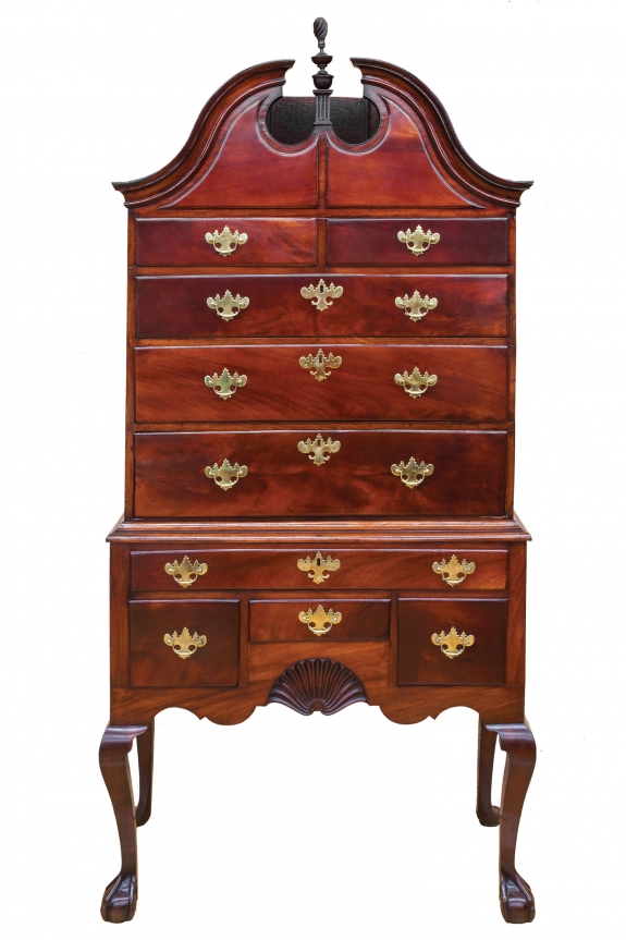An early Chippendale bonnet top highboy of striking Cuban mahogany with claw and ball feet and Newport shell, original finial, c. 1765. Provenance with Olney family of Providence/Newport. Attribution: John Goddard, based upon the John Brown chair sold at Christie&#039;s, January 2002, lot 351, related claw and ball feet modeling. Courtesy of The Stanley Weiss Collection.
